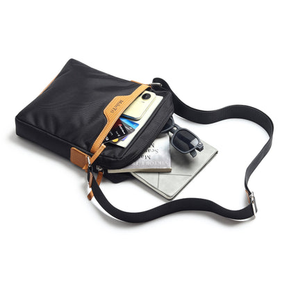 Black canvas crossbody bag with tan trim, open top showing phone and card pockets