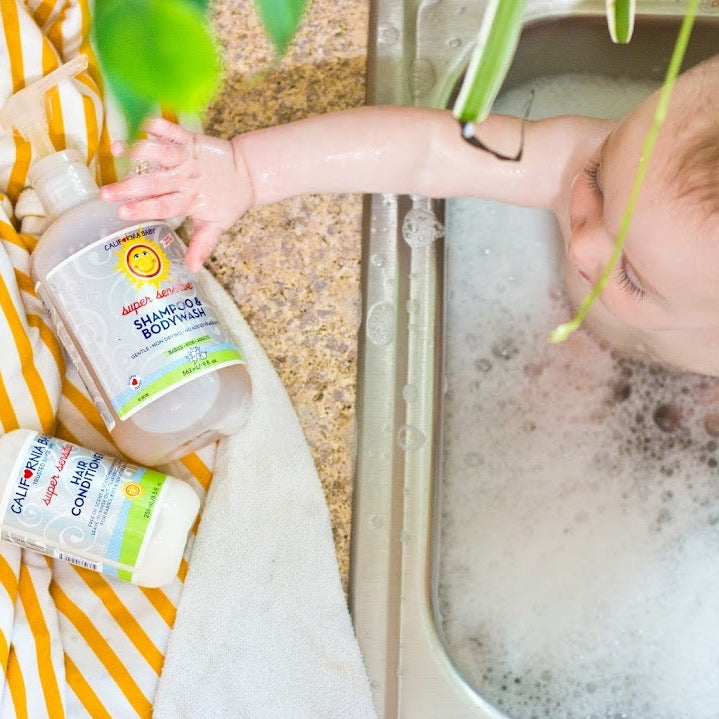 Super sensitive shampoo pump bottle beside conditioner in foamy bathwater