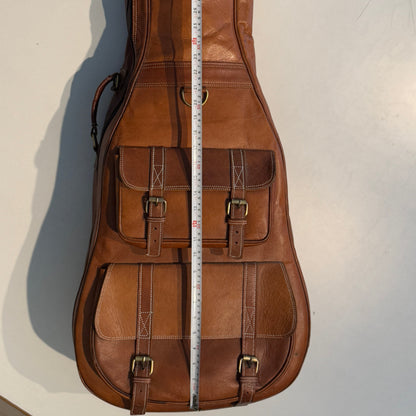 Brown leather guitar case with front buckled pockets and measuring tape at center.