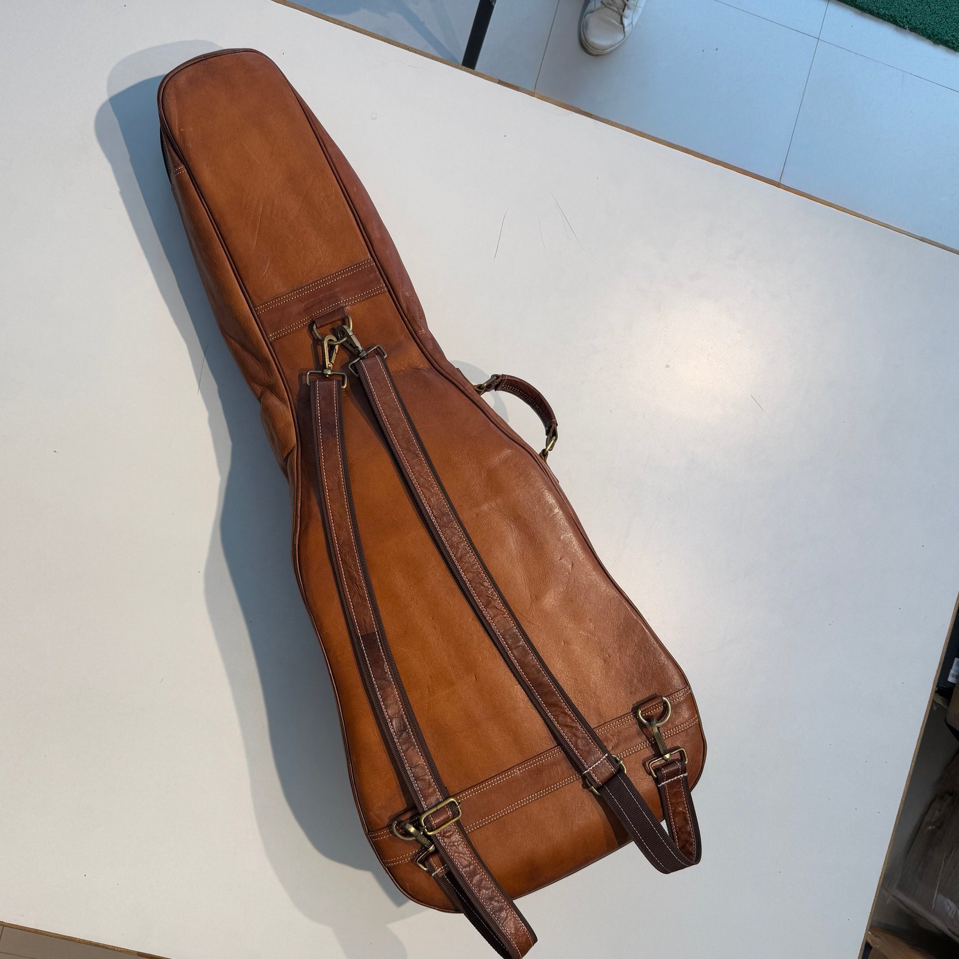 Brown leather guitar case with long shoulder strap and metal buckles