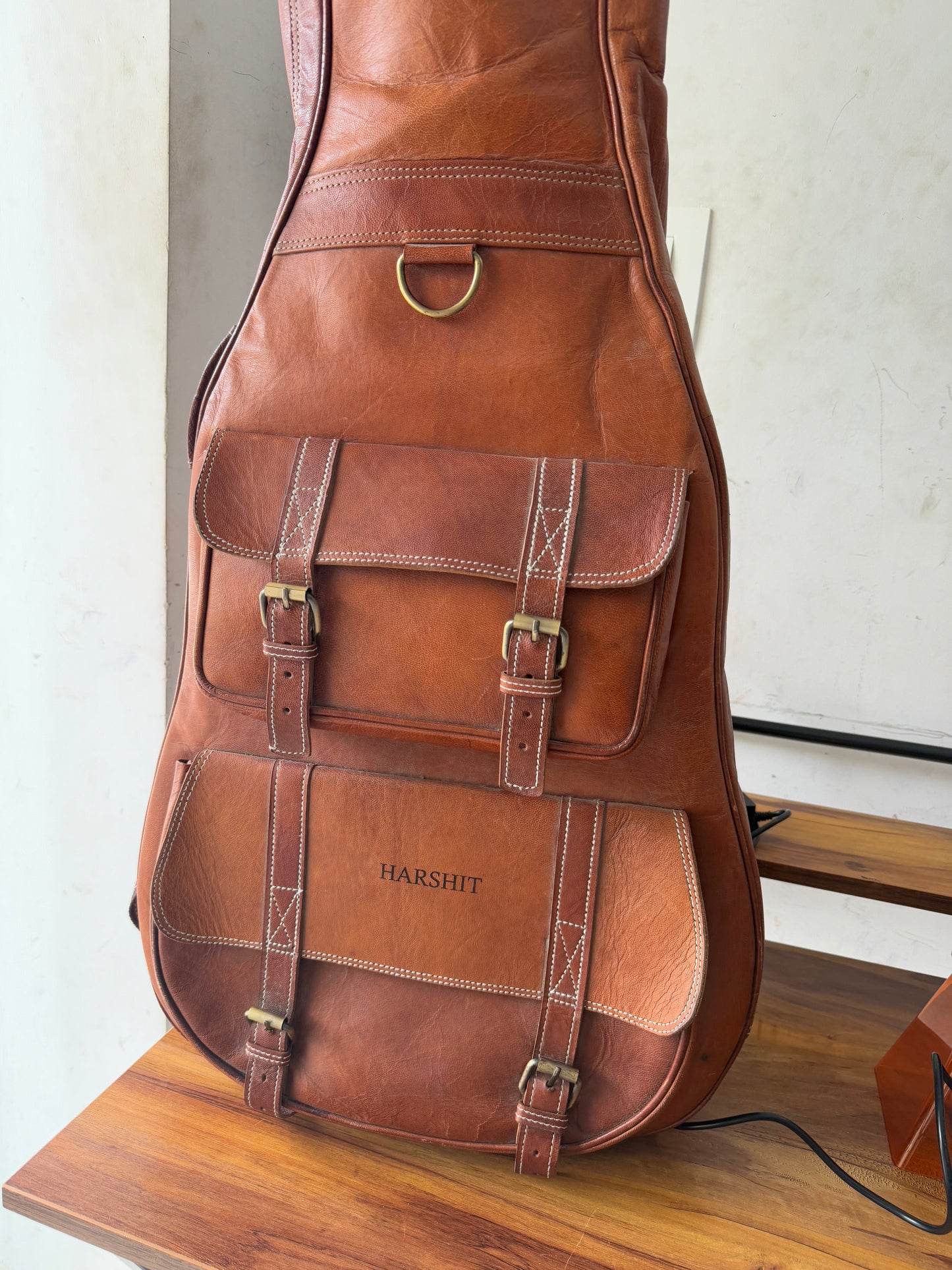 Brown leather guitar case with front buckled compartments and top handle, on display.