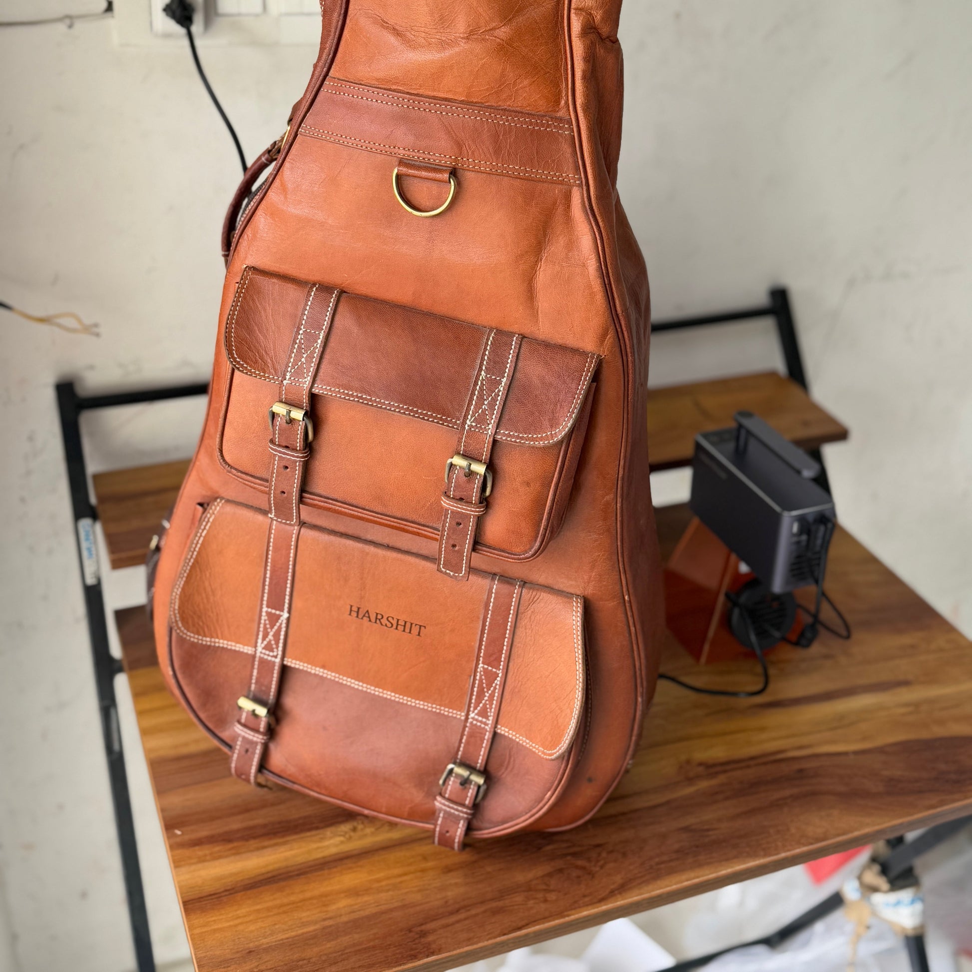 Brown leather guitar case with front latch, stitched panels, and buckled straps