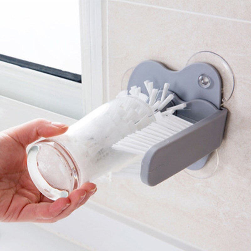 Gray kitchen bottle brush with white bristles and wall-mounted holder, bottle being cleaned