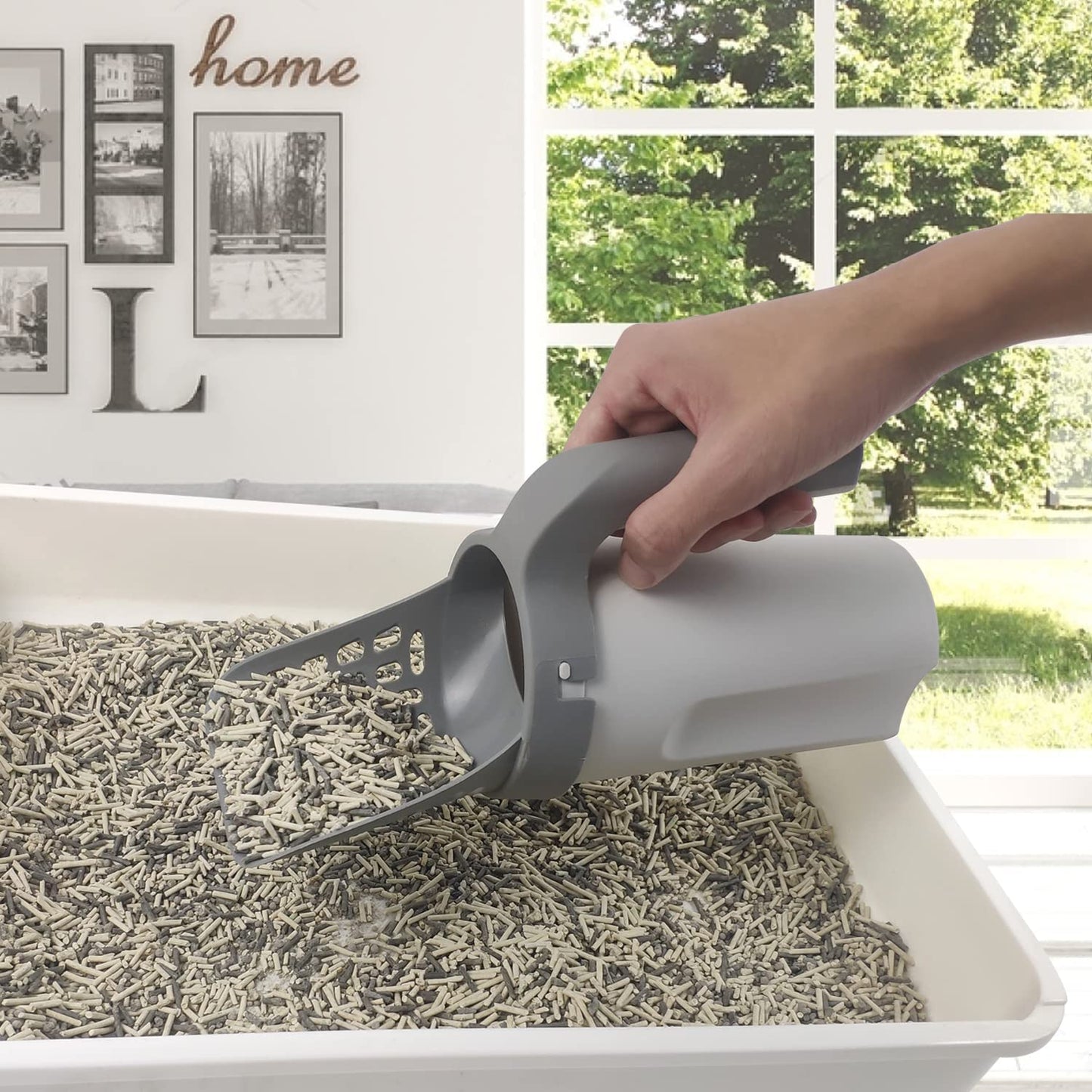 Cat litter scoop in hand over litter tray with gray perforated sifter