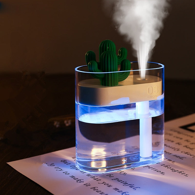 Clear ultrasonic air humidifier with green cactus top, emitting a vertical mist plume