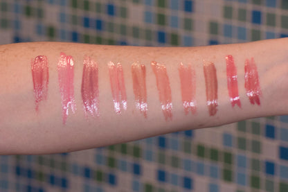 Glossy lip and color swatches on a forearm, glossy streaks in pink and nude tones.