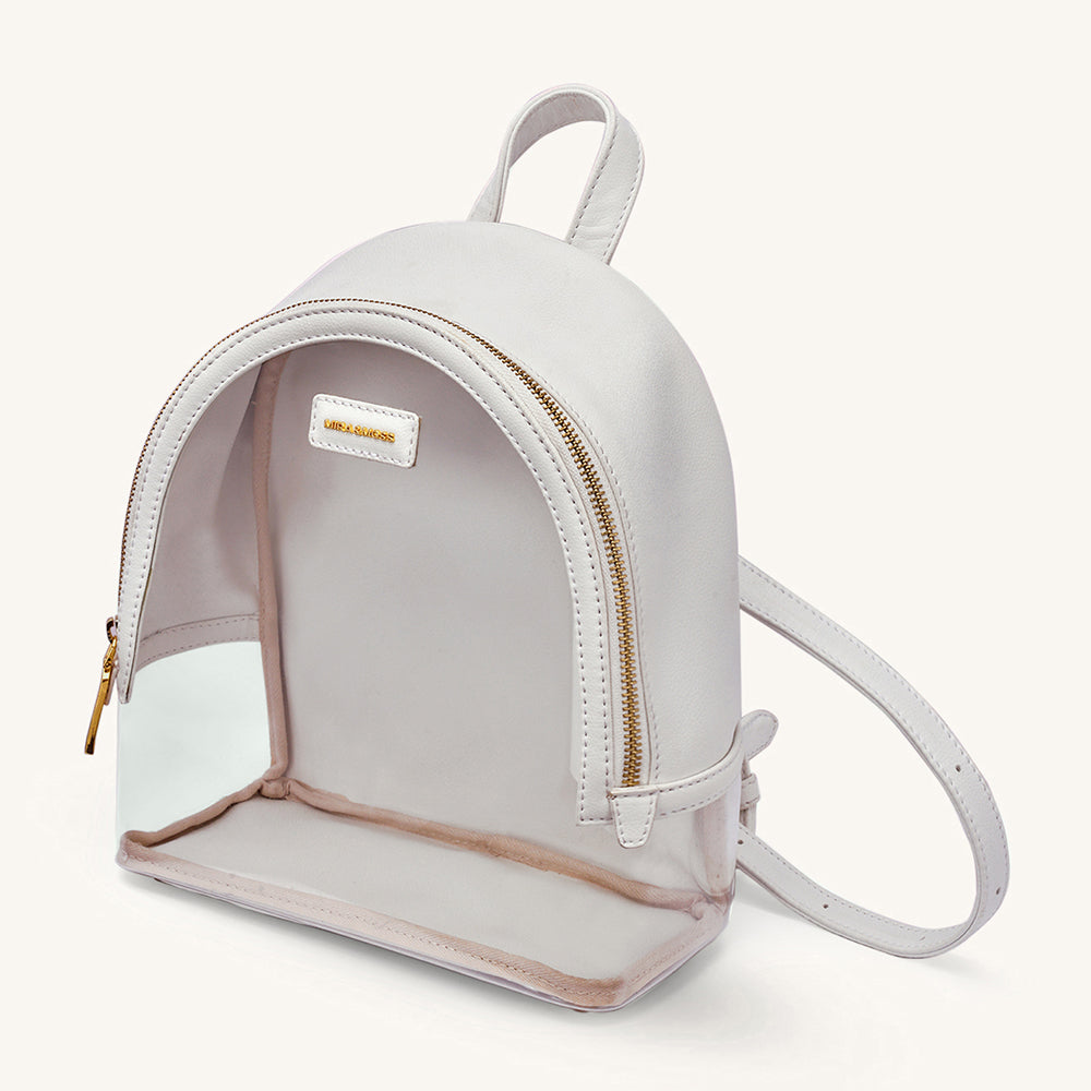 Ivory clear-front mini backpack with gold zipper, logo patch, and crossbody strap