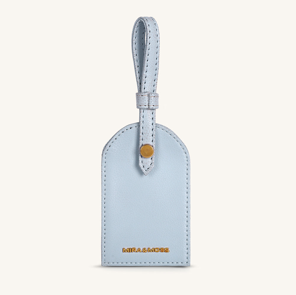 Ice blue leather travel tag with top loop and gold snap detail, stitched edges