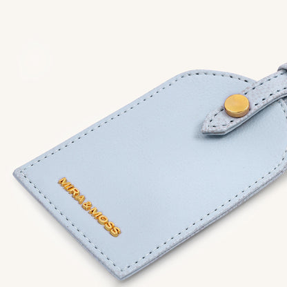 Ice blue travel tag close-up with gold MIRA&MESS logo and stitched border