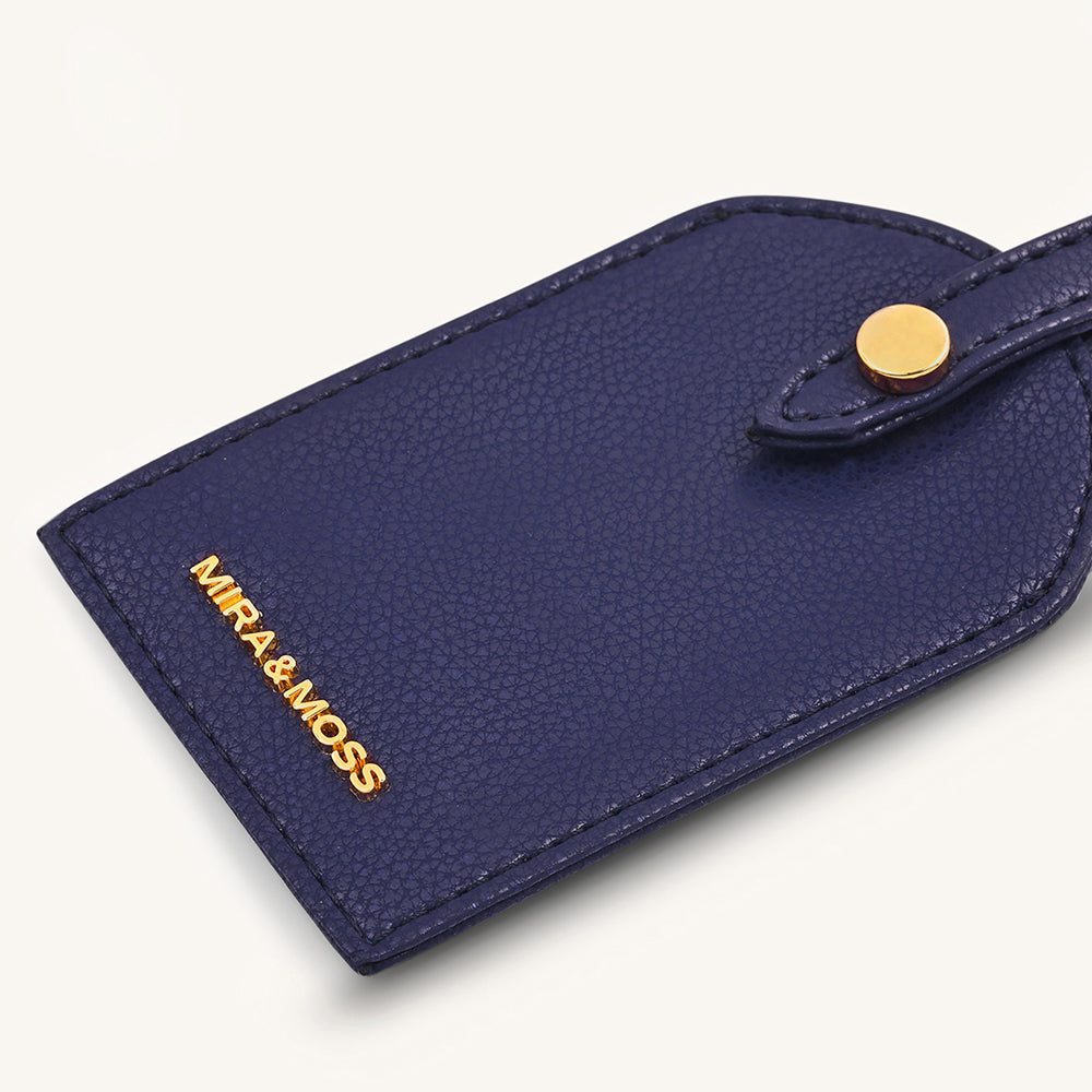 Dark blue travel tag front close-up with MIRA&MOSS logo and gold snap