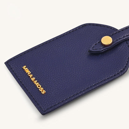 Dark blue travel tag front close-up with MIRA&MOSS logo and gold snap