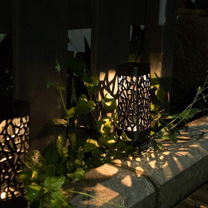 Black cutout solar garden light glowing beside stone edging