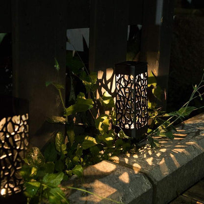 Black cutout solar garden light glowing beside stone edging