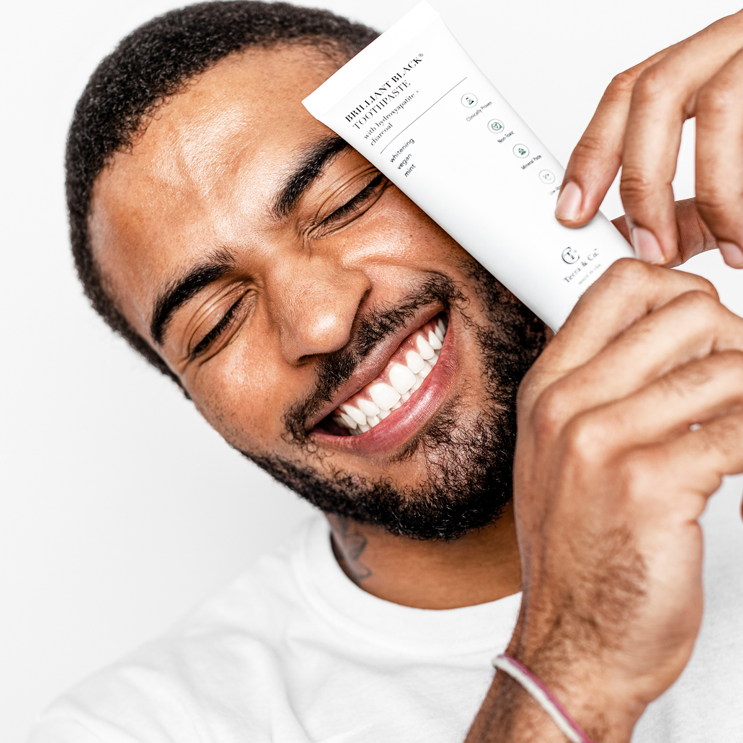 Toothpaste tube held near smiling man brushing teeth with mint paste