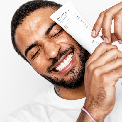 Toothpaste tube held near smiling man brushing teeth with mint paste