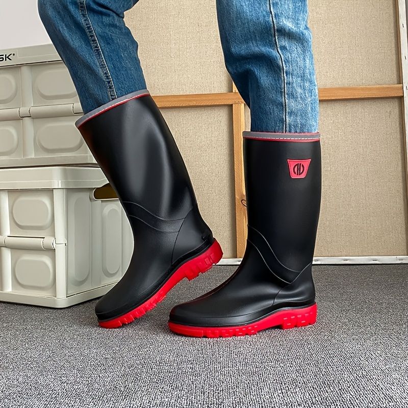 Black knee-high rain boots with red-trim collar worn with jeans; thick tread sole.