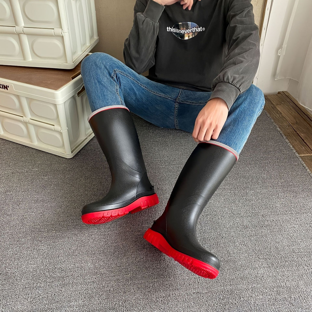 Knee-high black rain boots with red outsole, worn with blue jeans