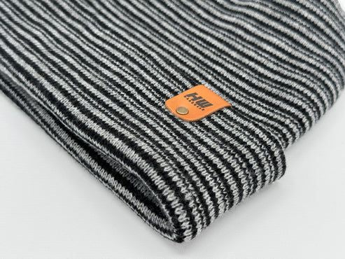 Rolled cuff of striped knit beanie in gray and black with orange logo patch