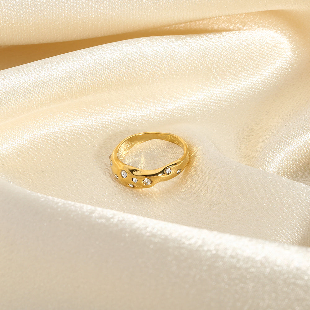 Gold snake-shape ring with clear stones, top view on light fabric