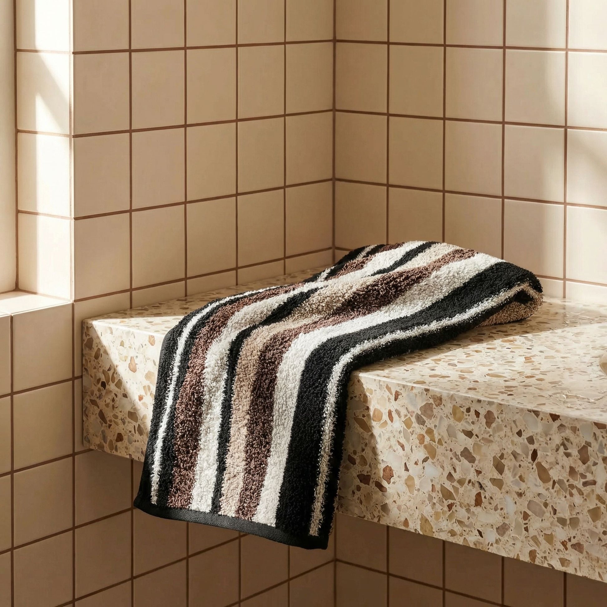 Striped towel draped over ledge, black and cream bands, plush terry.