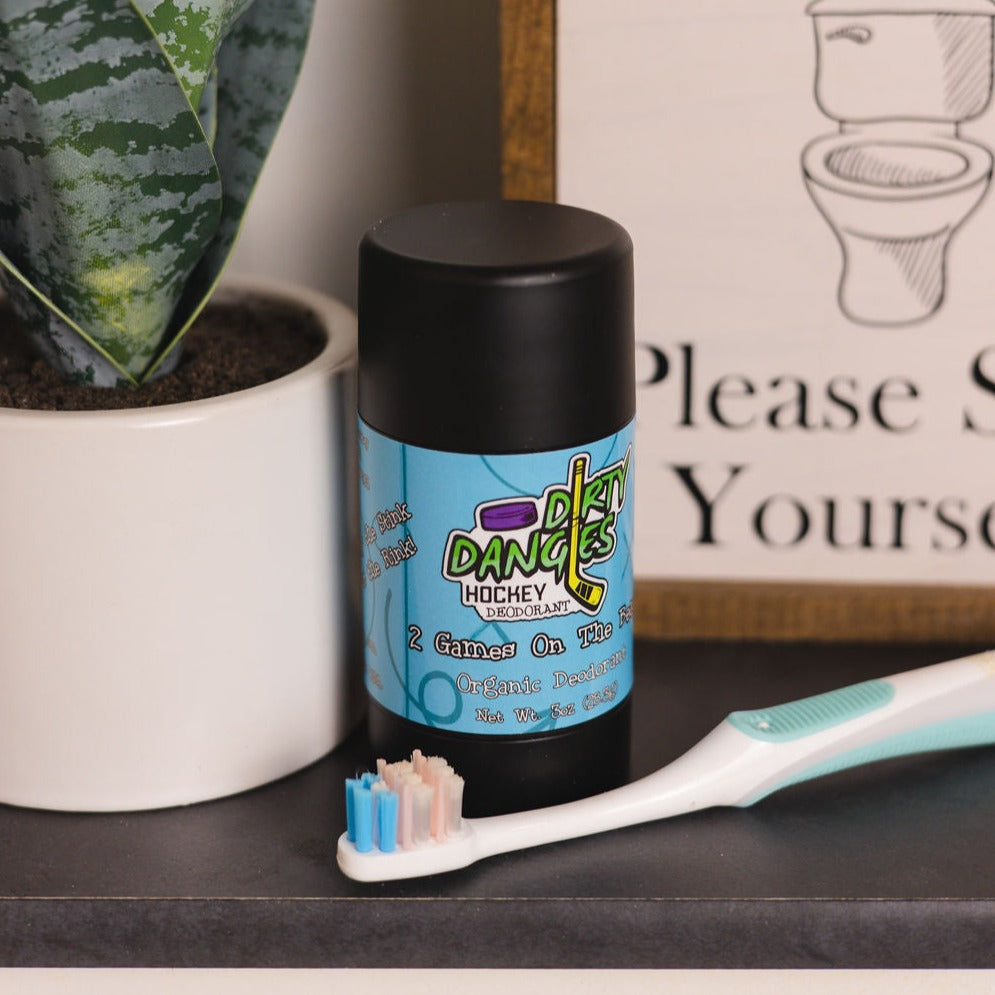 Natural deodorant bottle with black cap beside toothbrush and cup on countertop.