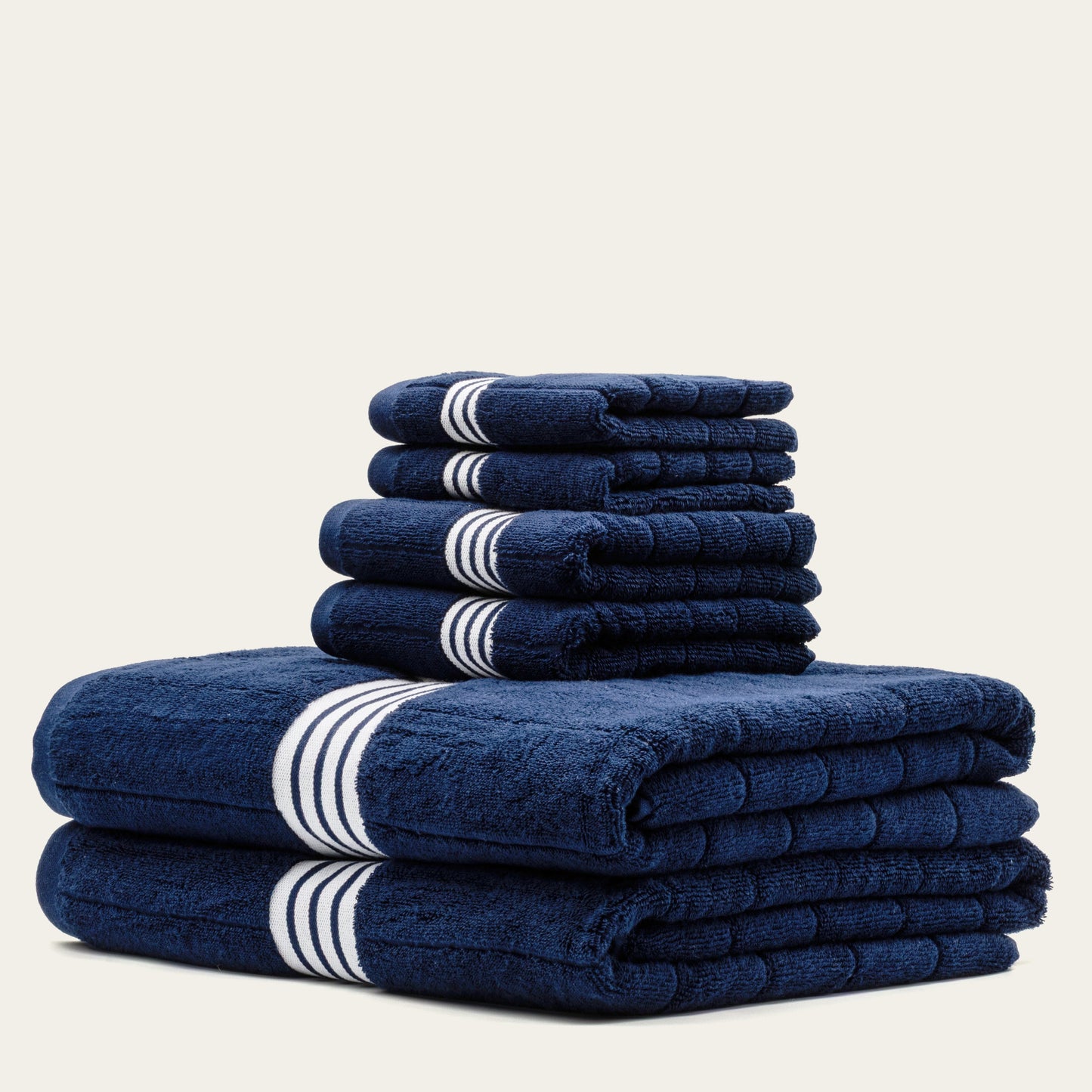 Navy cotton towels set with white striped bands, stacked in a high folded pile.