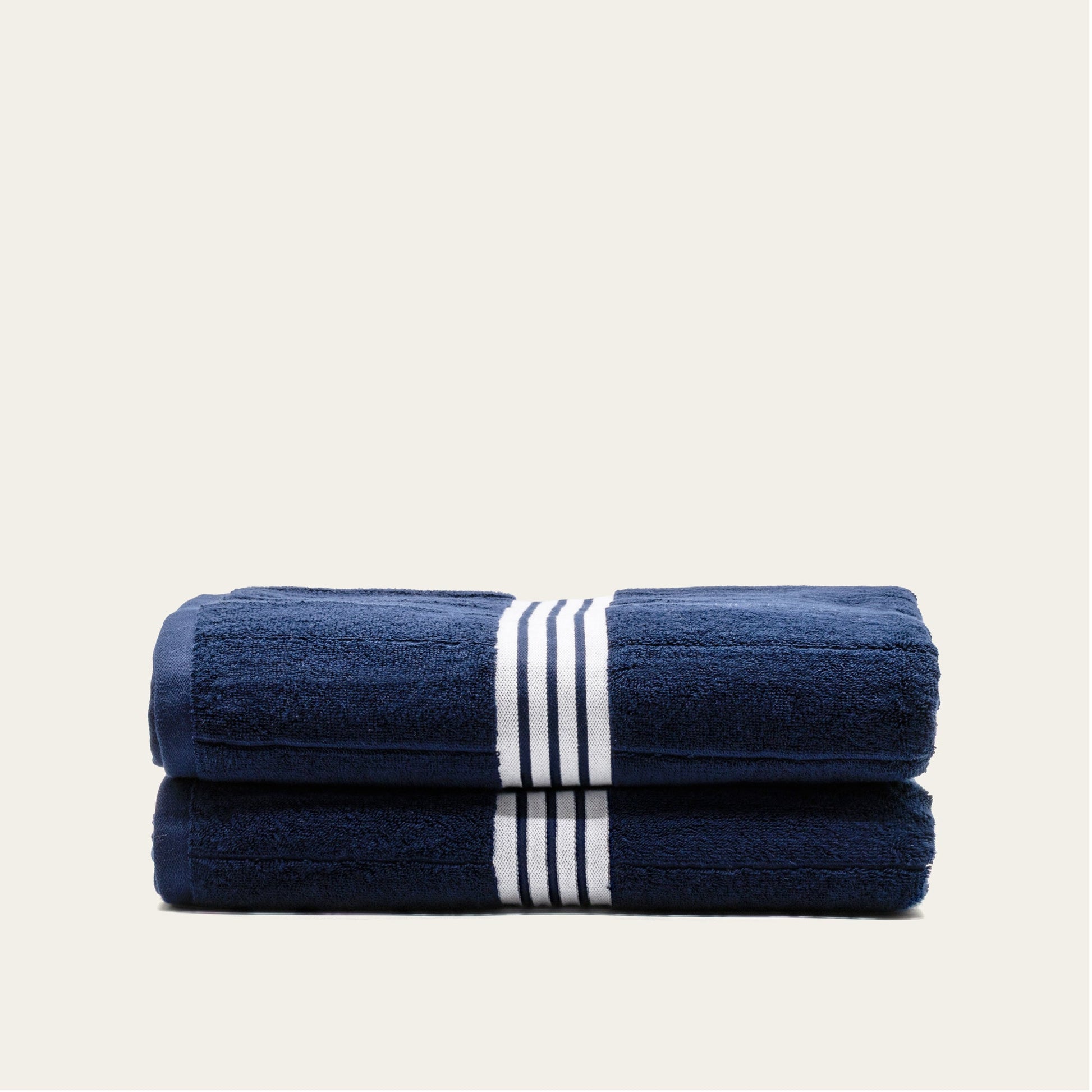 Navy cotton towels set with white striped bands, two rolled folds with a vertical stripe detail.
