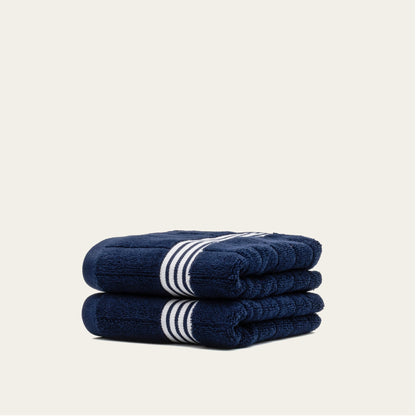 Navy cotton towels set with white striped bands, two folded towels stacked with rounded edges.