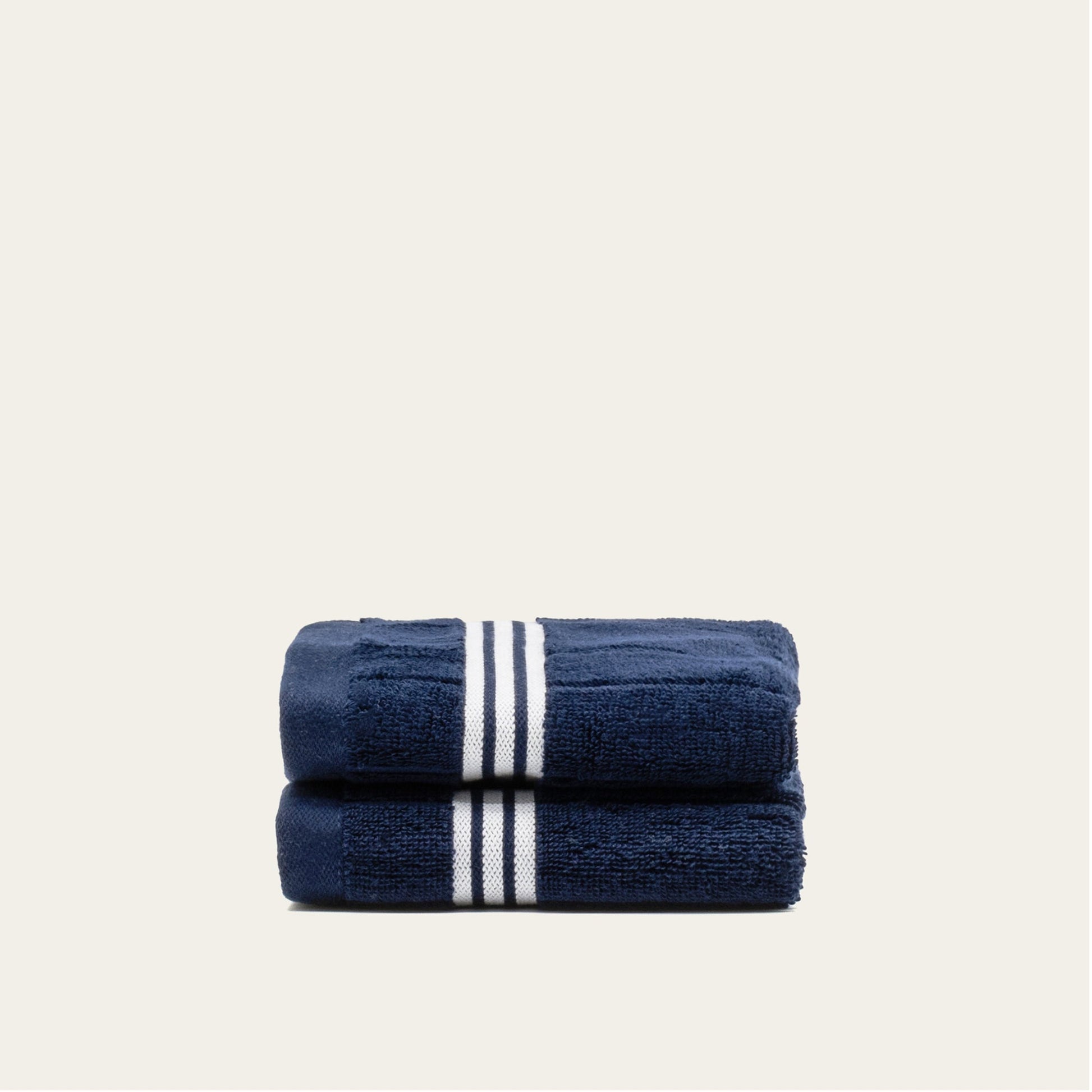 Navy cotton towels set with white triple stripe bands, stacked and folded.