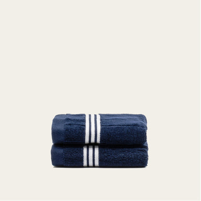 Navy cotton towels set with white triple stripe bands, stacked and folded.