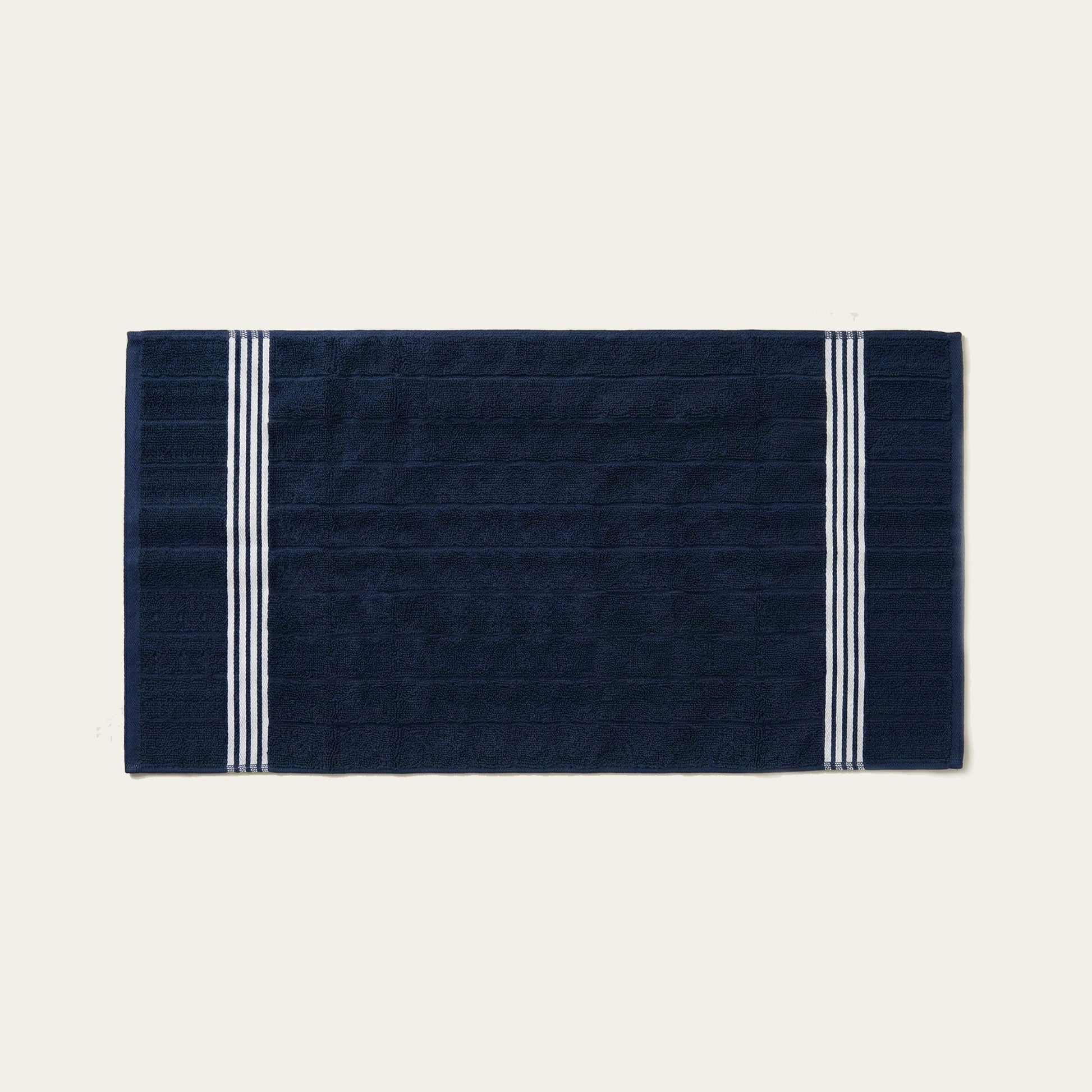 Navy cotton towel with white triple stripe bands along the edges, folded flat.