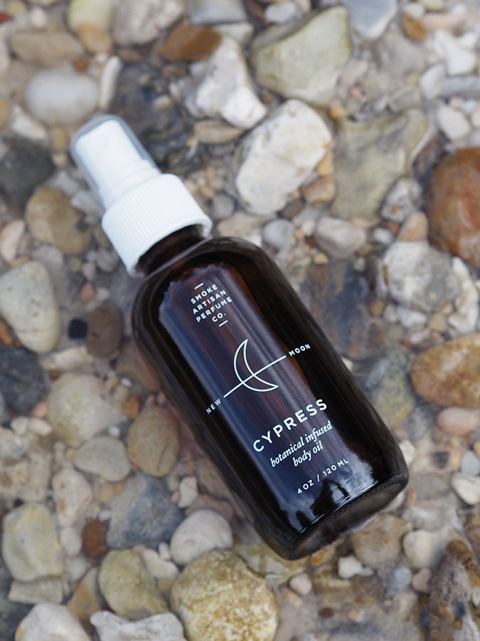 Cypress body oil bottle with white spray cap, dark amber glass on rocks