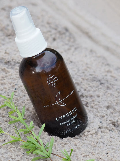 Cypress body oil bottle with white spray cap and amber glass, on light stone