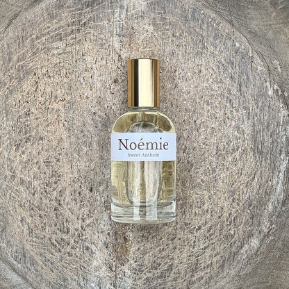 Noémie perfume bottle with gold cap, clear glass, label 'Sweet Anthem'.