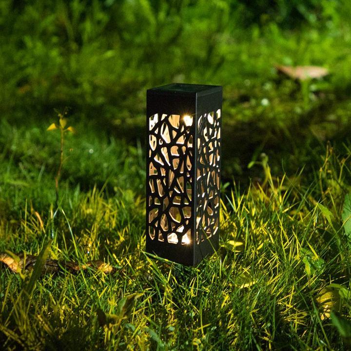 Black cutout solar garden light with warm glow on grass