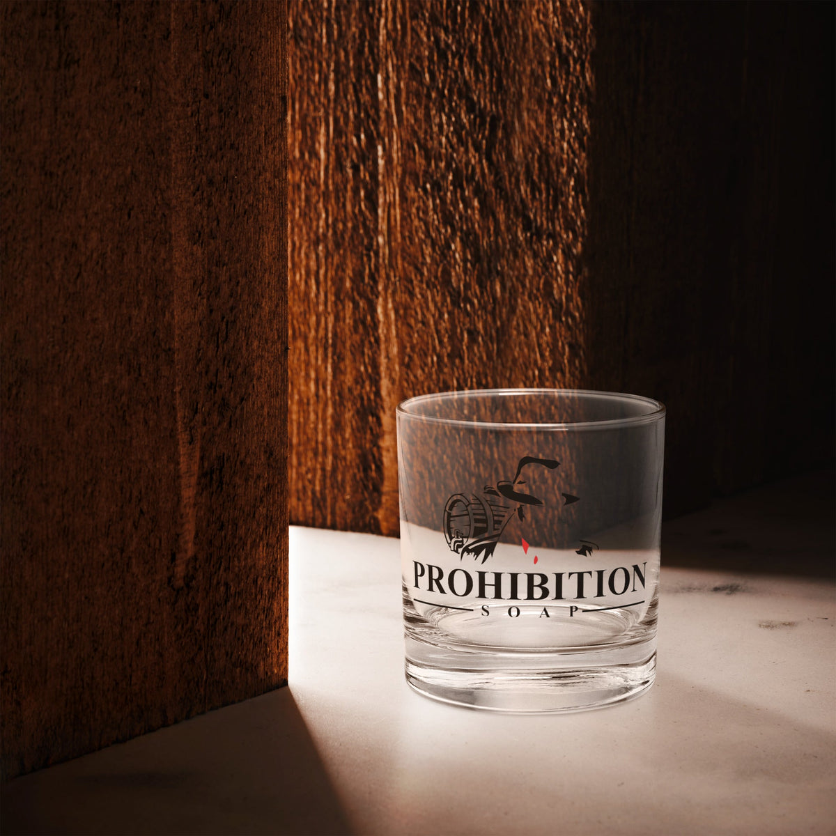 Clear glass tumbler with black logo graphic and orange band along the bottom
