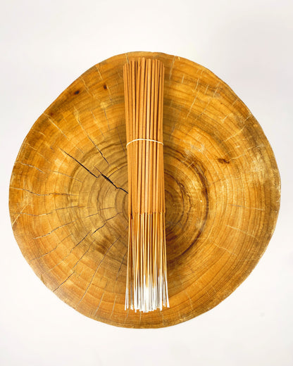 Incense stick bundle with white sticks standing in a round wooden dish