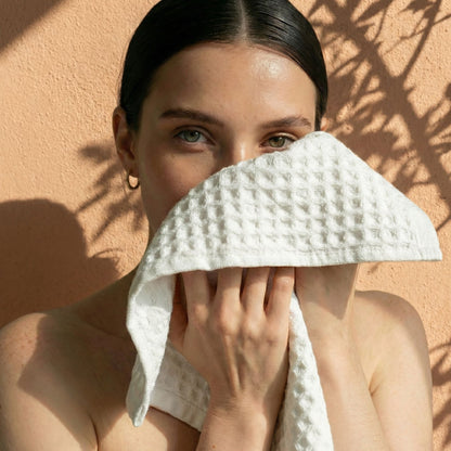 White waffle cotton towel held to face, textured waffle weave and soft folds.
