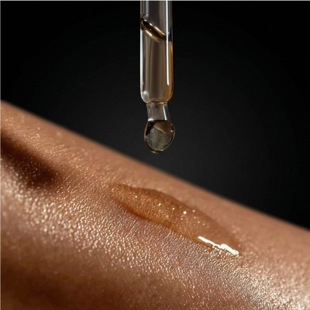 Dropper releasing shimmer body oil onto skin, creating a glossy line