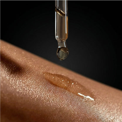 Dropper releasing shimmer body oil onto skin, creating a glossy line