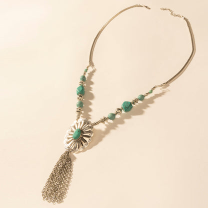 Pendant necklace with turquoise green beads, silver sunburst charm, and tassel