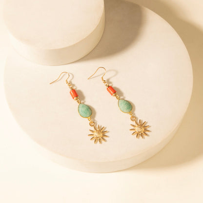Gold-tone drop earrings with green teardrop stones, orange beads, and sunburst charms.