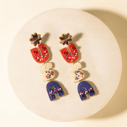 Beaded charm earrings with red, white, and blue shapes and gold-tone tops; dangling.