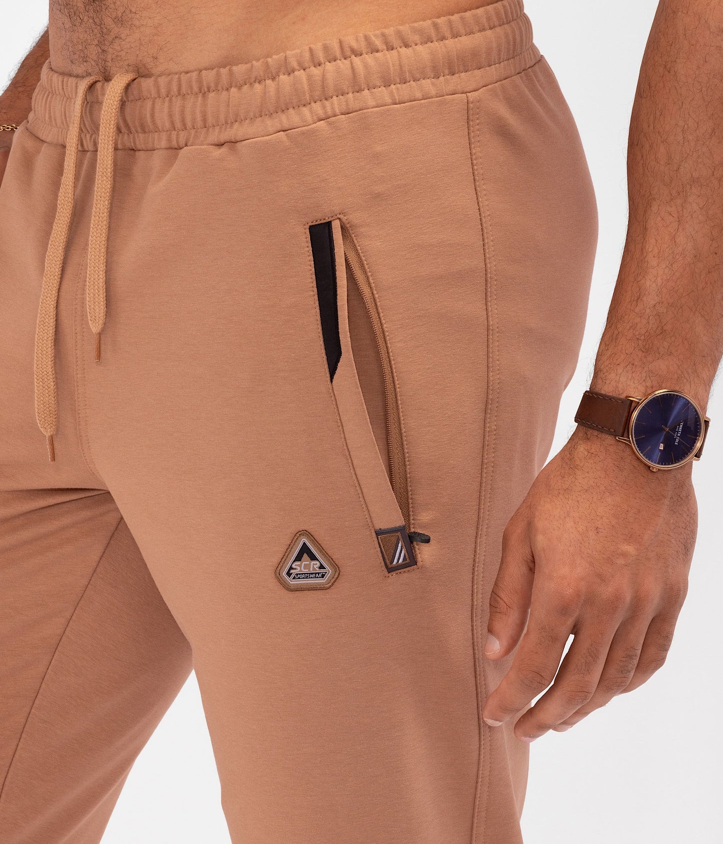 Rust-brown athletic sweatpants close-up showing zip pocket, drawstring, and cuffed legs