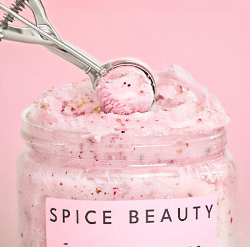 Scoop of pink exfoliating body scrub in jar with dark specks