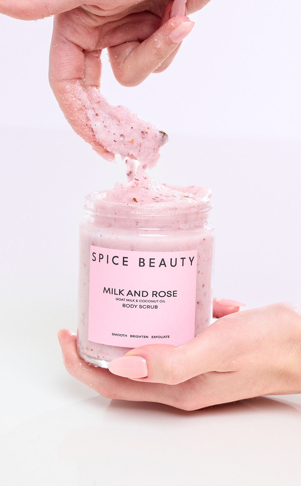Body scrub jar held in hands with thick pink exfoliating scrub