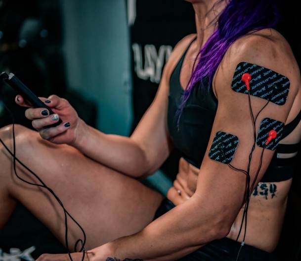 Muscle stimulator electrode pads on forearm and shoulder with connected wires