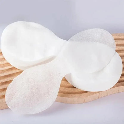 Two white disposable eye pads with curved shape on a wooden surface