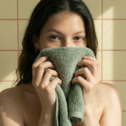 Green plush towel held to face, close-up of terry texture