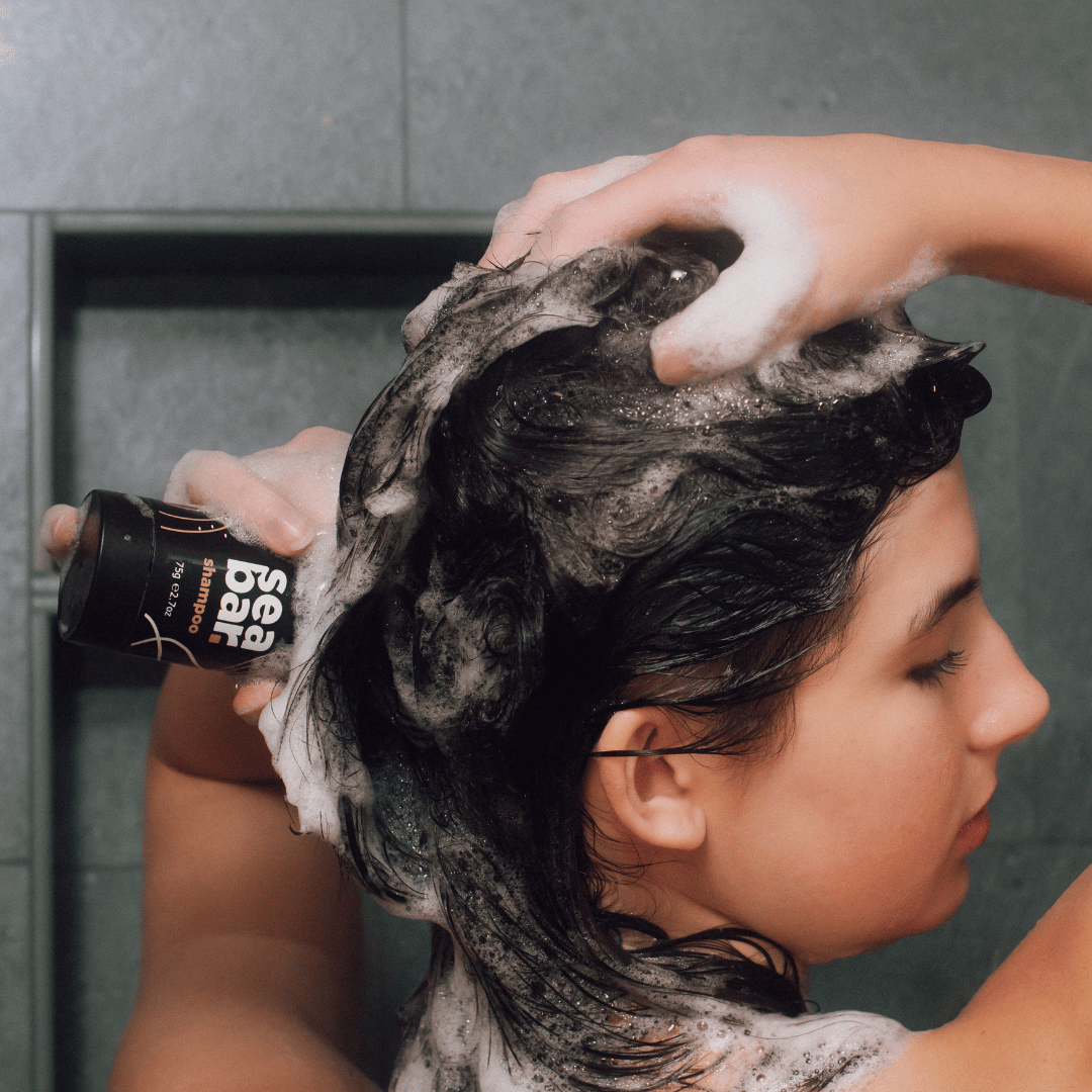 Shampoo bar lather on dark hair while squeezing product bottle